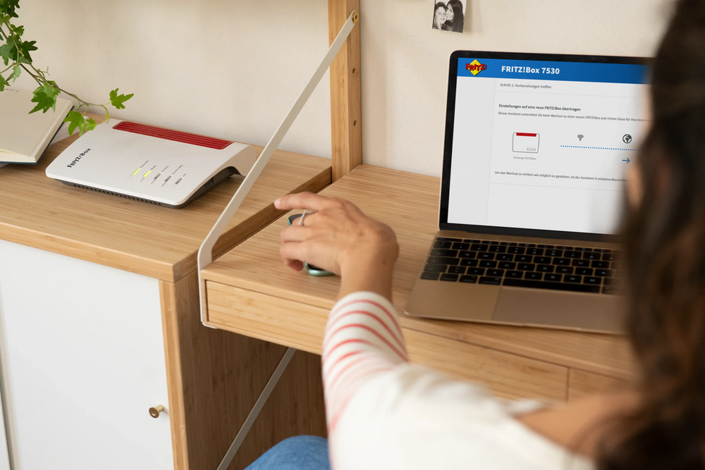 Person am Schreibtisch mit Laptop und FRITZ!Box 7530, WLAN-Einstellungen auf dem Bildschirm.