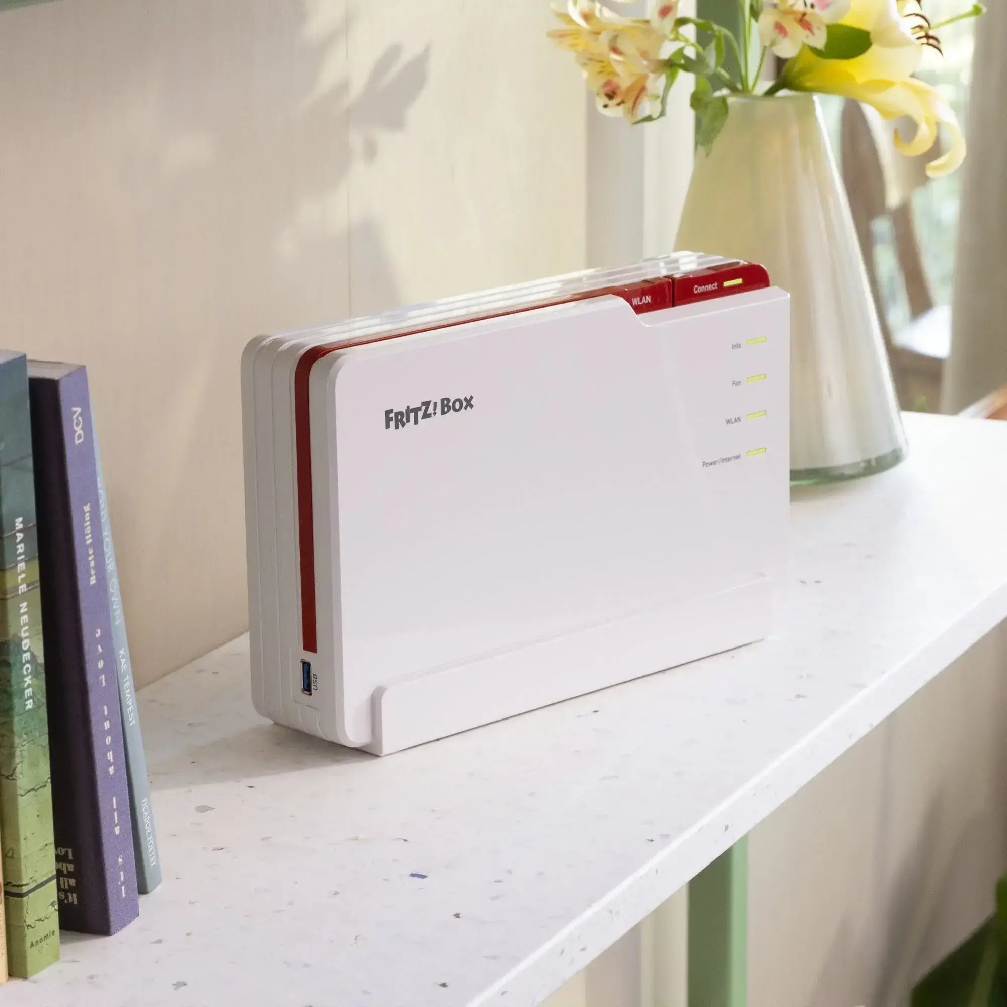 FRITZ!Box Router auf einem Regal, umgeben von Büchern und Blumen, für schnelles WLAN zu Hause.