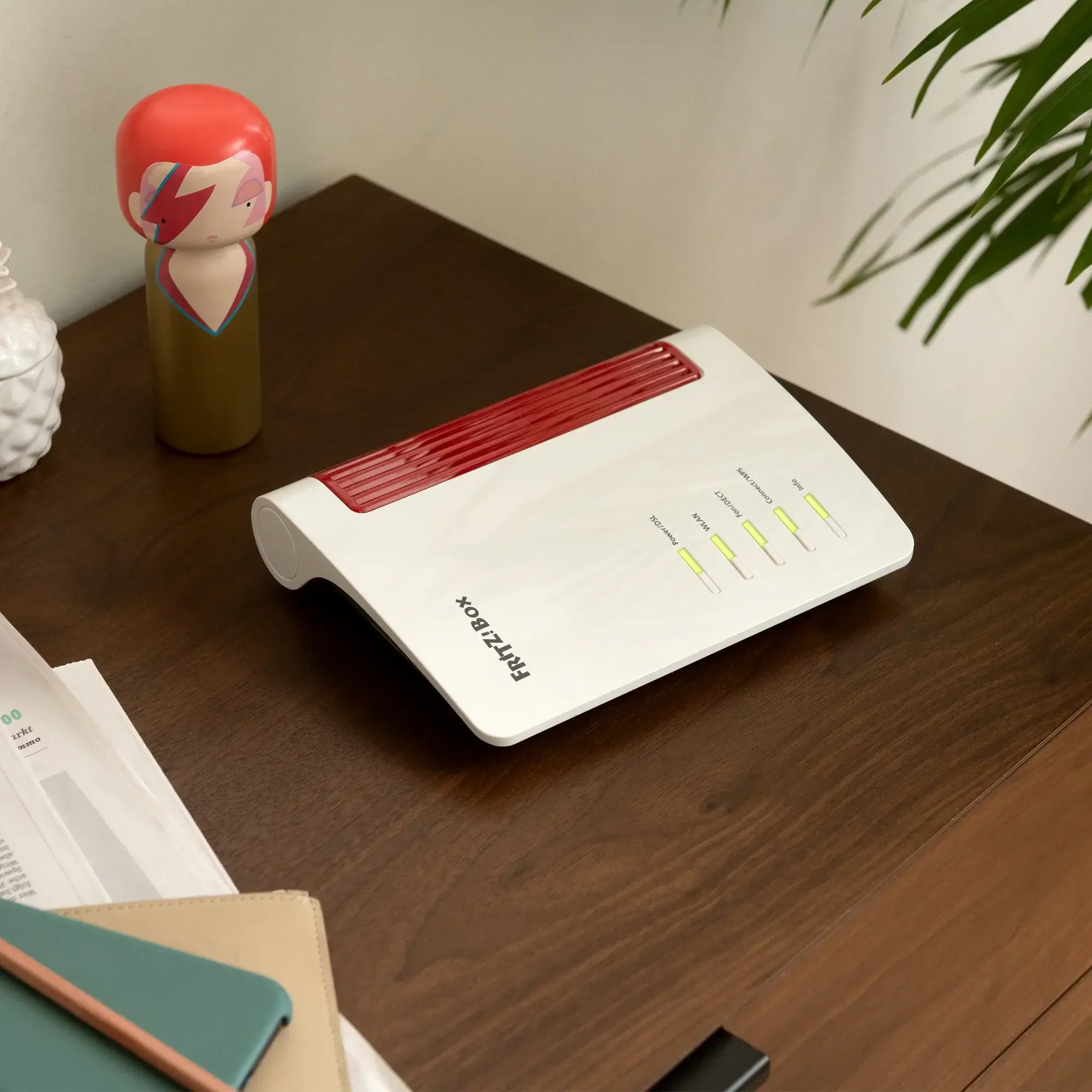 Moderne FRITZ!Box auf einem Holztisch, daneben eine verspielte Figur, ideal für Heimnetzwerke.