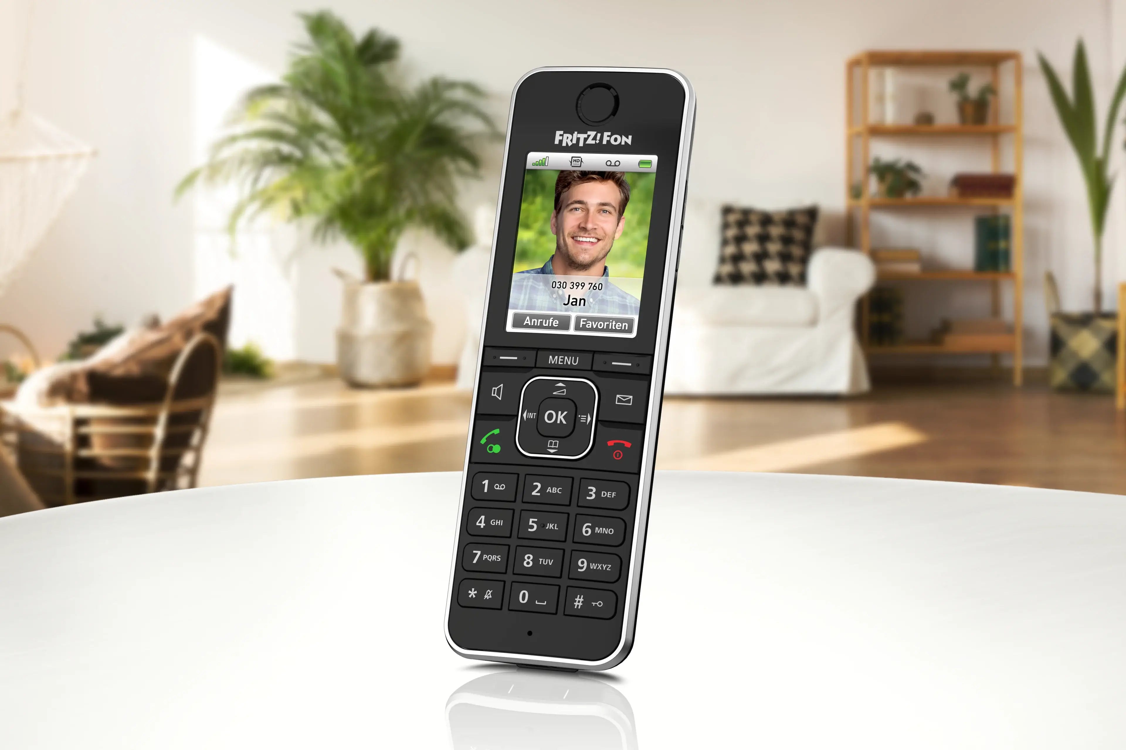 Fritz Fon Telefon mit Bildschirm und Tasten, steht auf einem Tisch in einem modernen Wohnraum.