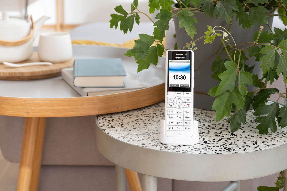 Moderne Telefon auf einem Tisch mit Pflanzen und Büchern, ideal für Zuhause oder Büro. Anzeige zeigt 10:30.