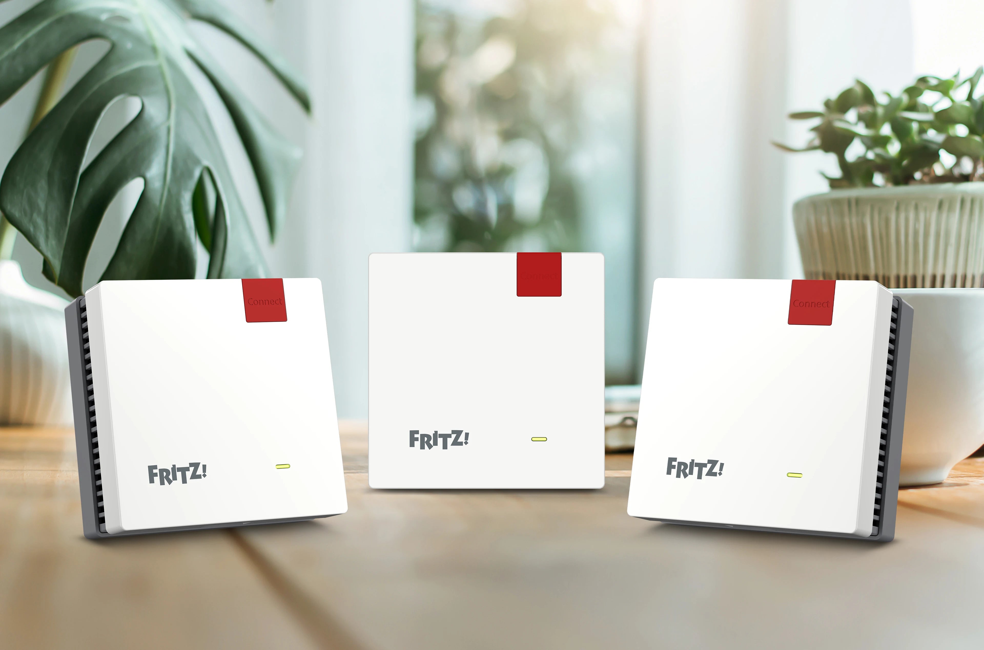 Drei FRITZ!Box Geräte in einem hellen Raum mit Pflanzen im Hintergrund, ideal für schnelles Internet.
