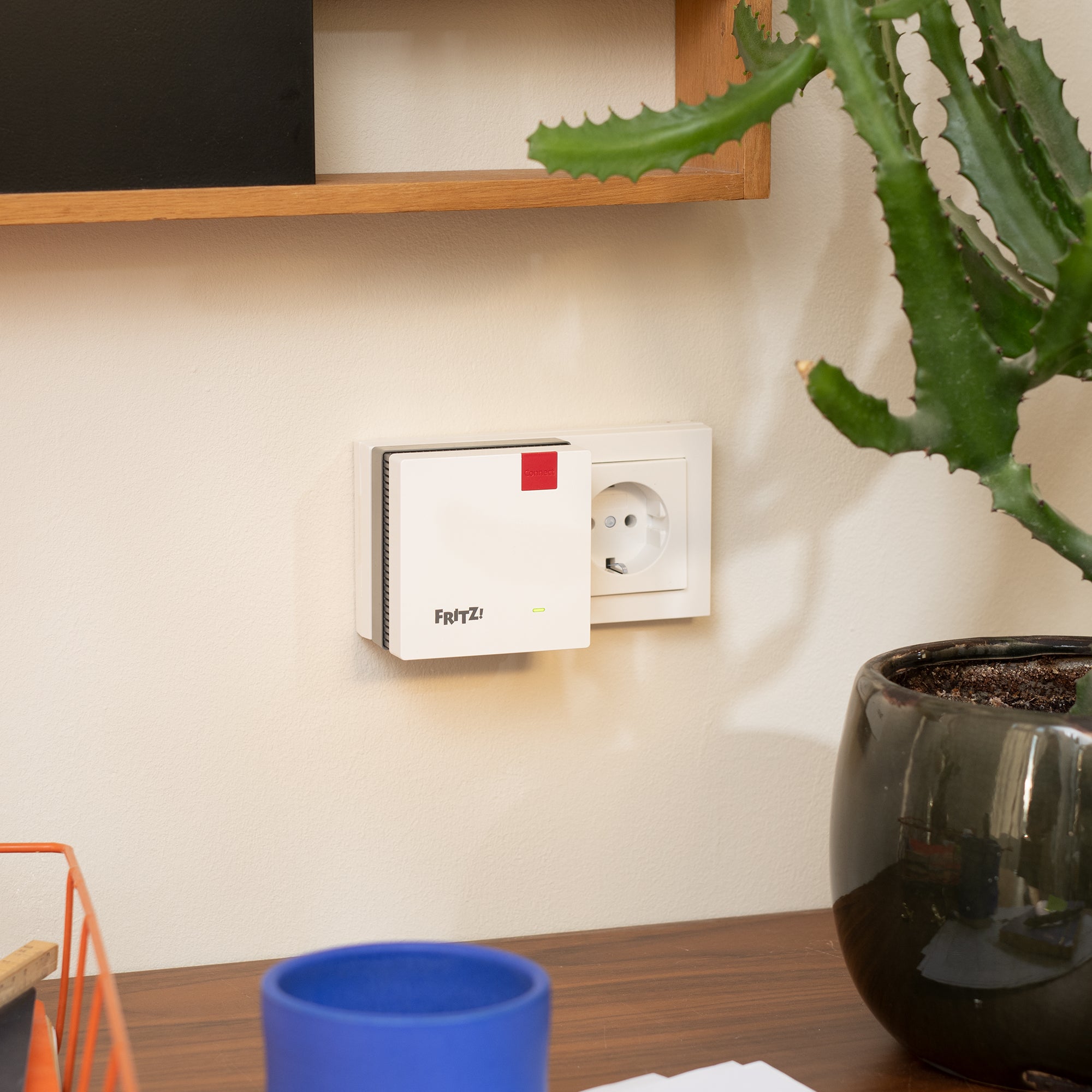 FRITZ!Repeater 1200 AX montiert an der Wand in einem modernen Raum mit grüner Pflanze und blauer Tasse