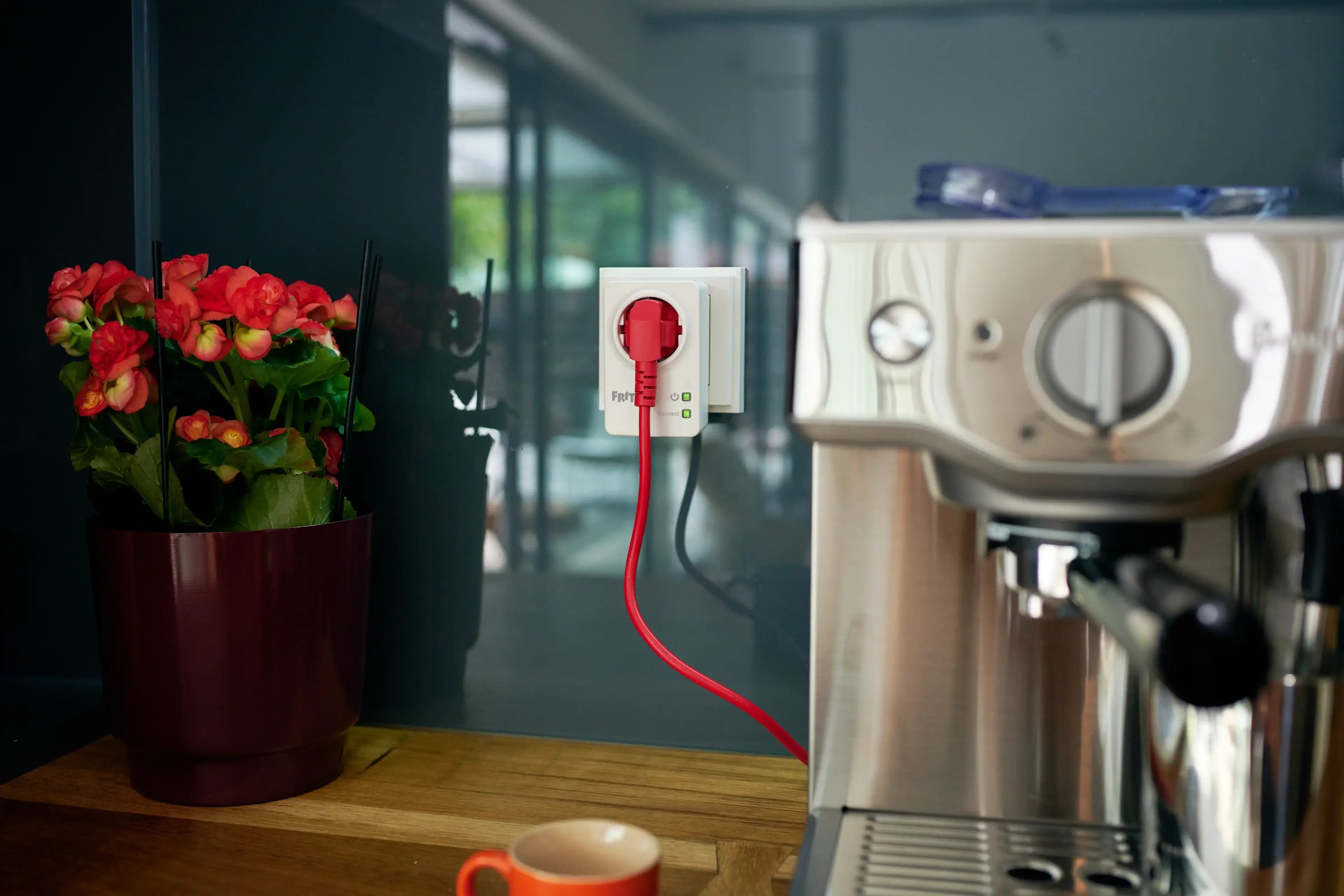 Rote Steckdose mit Kabel, Kaffeemaschine und Blumenpflanze auf Holztheke in modernen Kaffee-Ambiente.