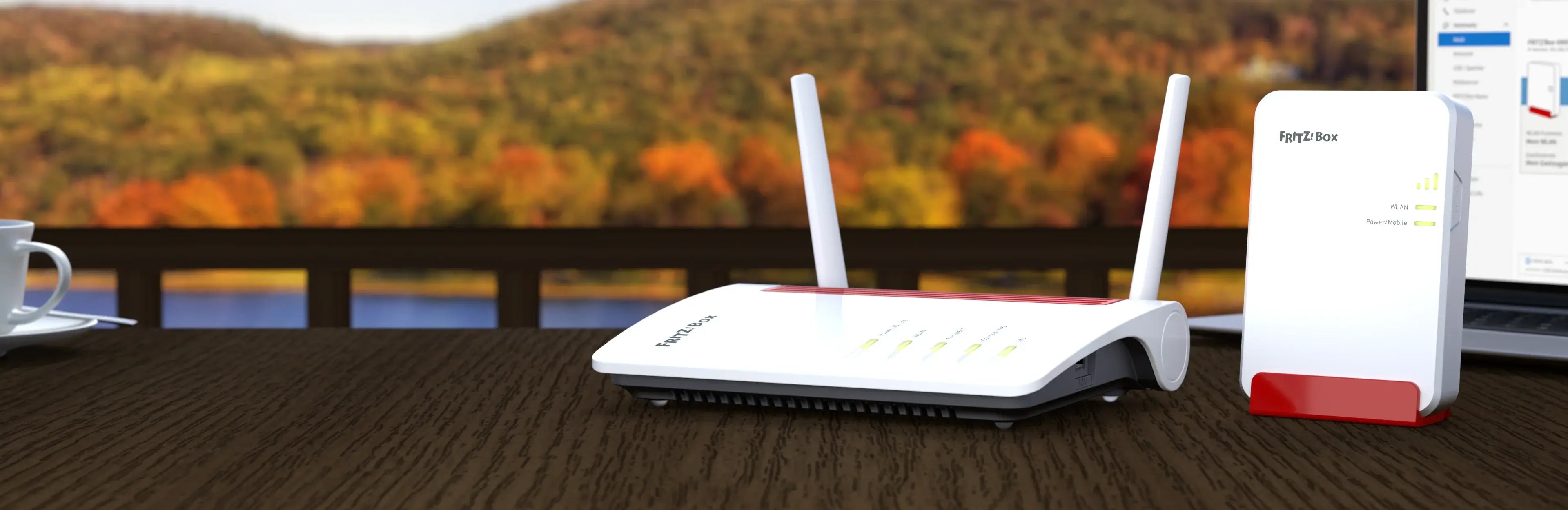 Router und Repeater auf einem Tisch mit herbstlicher Landschaft im Hintergrund, verbunden mit Laptop und Tasse.